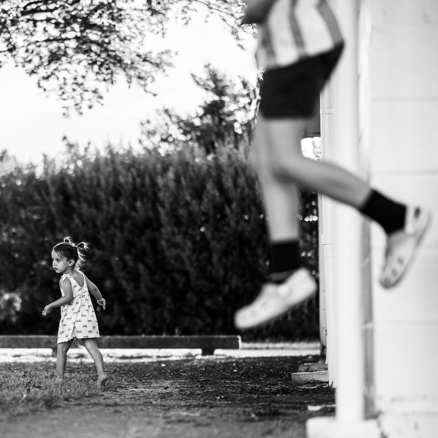 A little girl running past a leaping child, in black and white