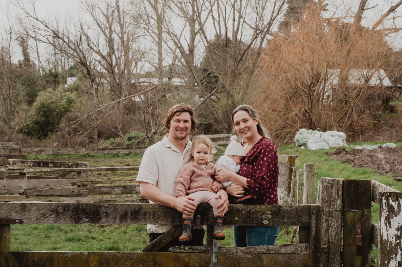 A couple and their baby sitting on a wooden fence in a paddock